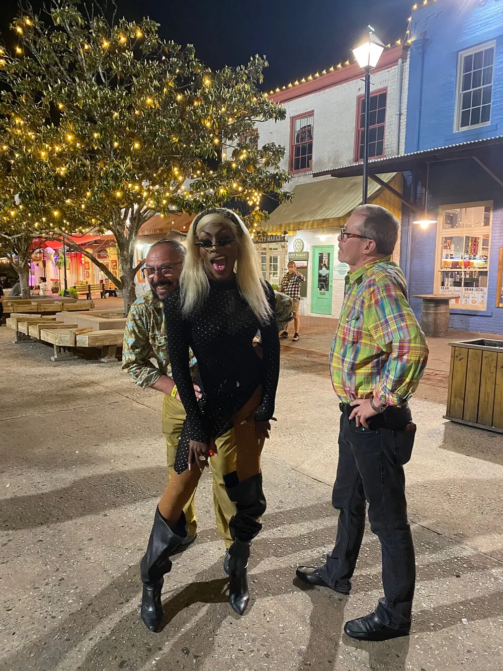 Three people are sharing a joyful moment on a lively street at night with one person playfully sticking out their tongue adding a hint of whimsy to the scene
