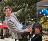 A person is playfully posed on a pole next to a mannequin dressed in a sparkling black outfit with outdoor dining and string lights in the background
