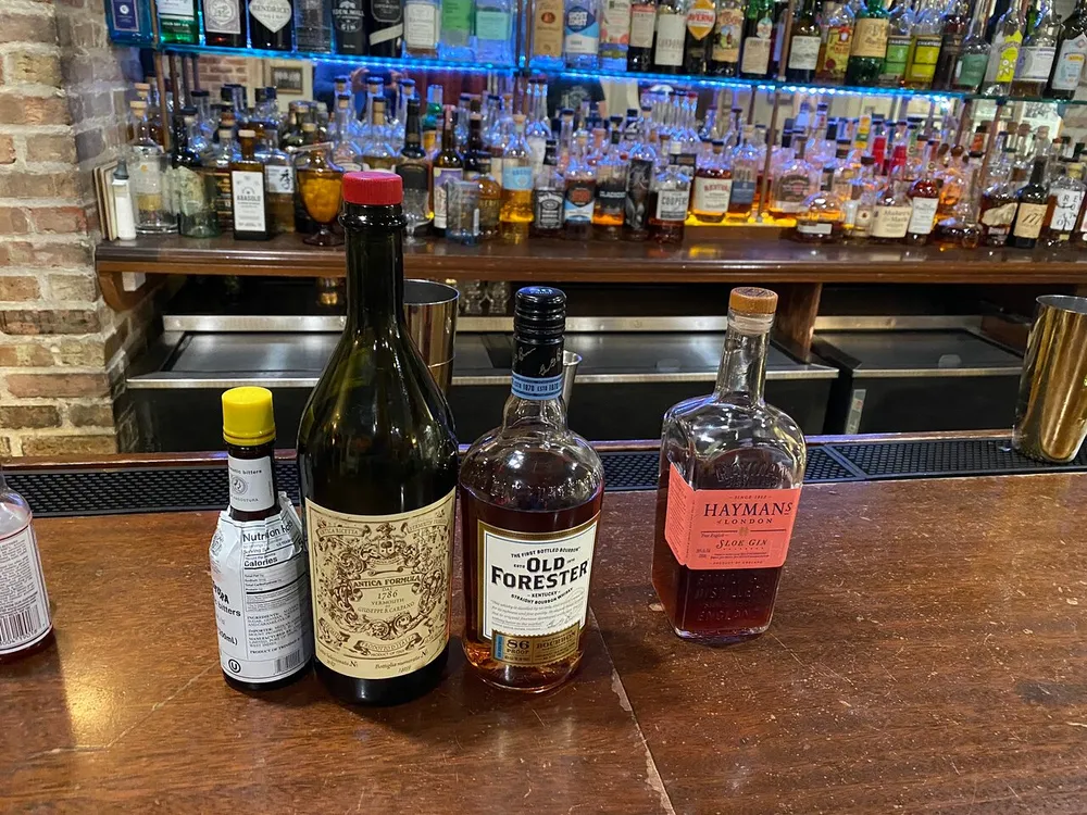 Three bottles of alcoholvermouth bourbon and ginare prominently displayed on a bar counter with an array of spirits in the background