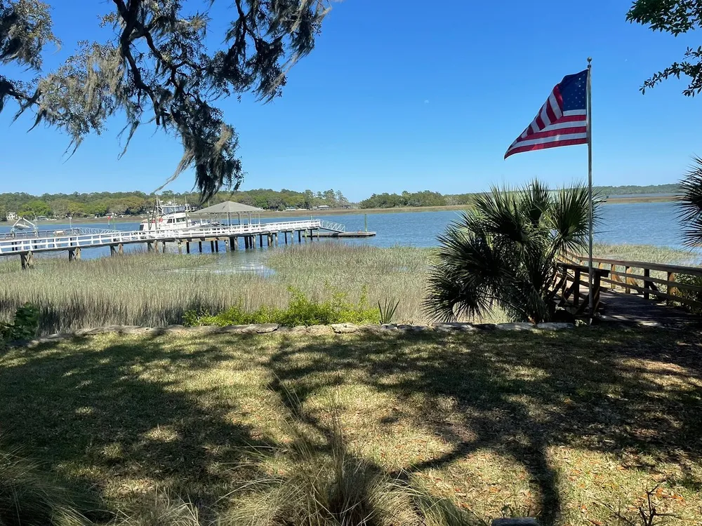 The image shows a serene waterfront scene with a dock a waving American flag and a lush landscape under a clear blue sky