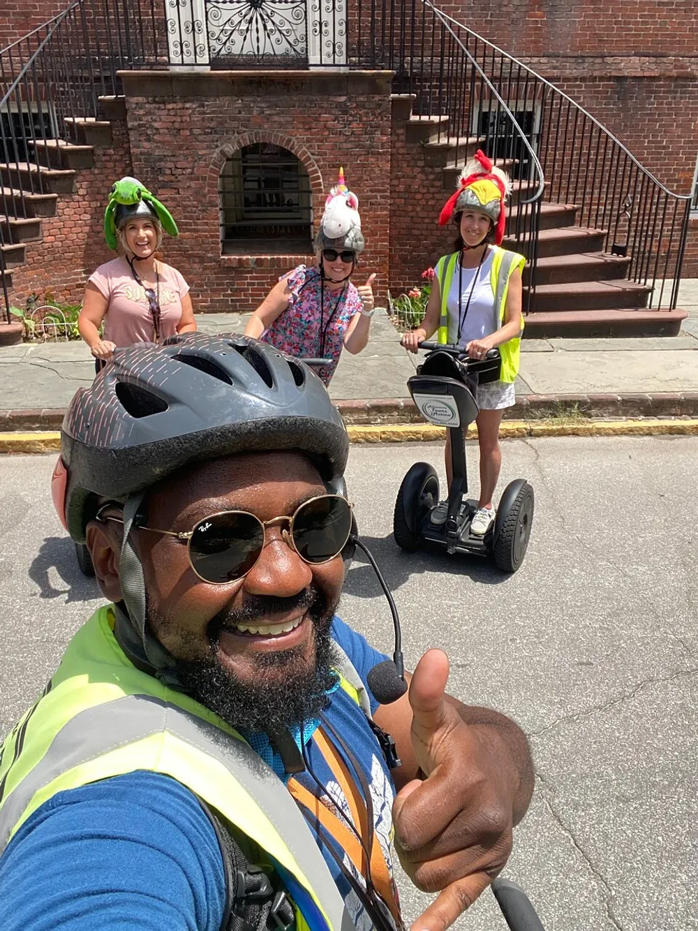 A cheerful group of people wearing fun helmets and safety gear takes a selfie while on a Segway tour