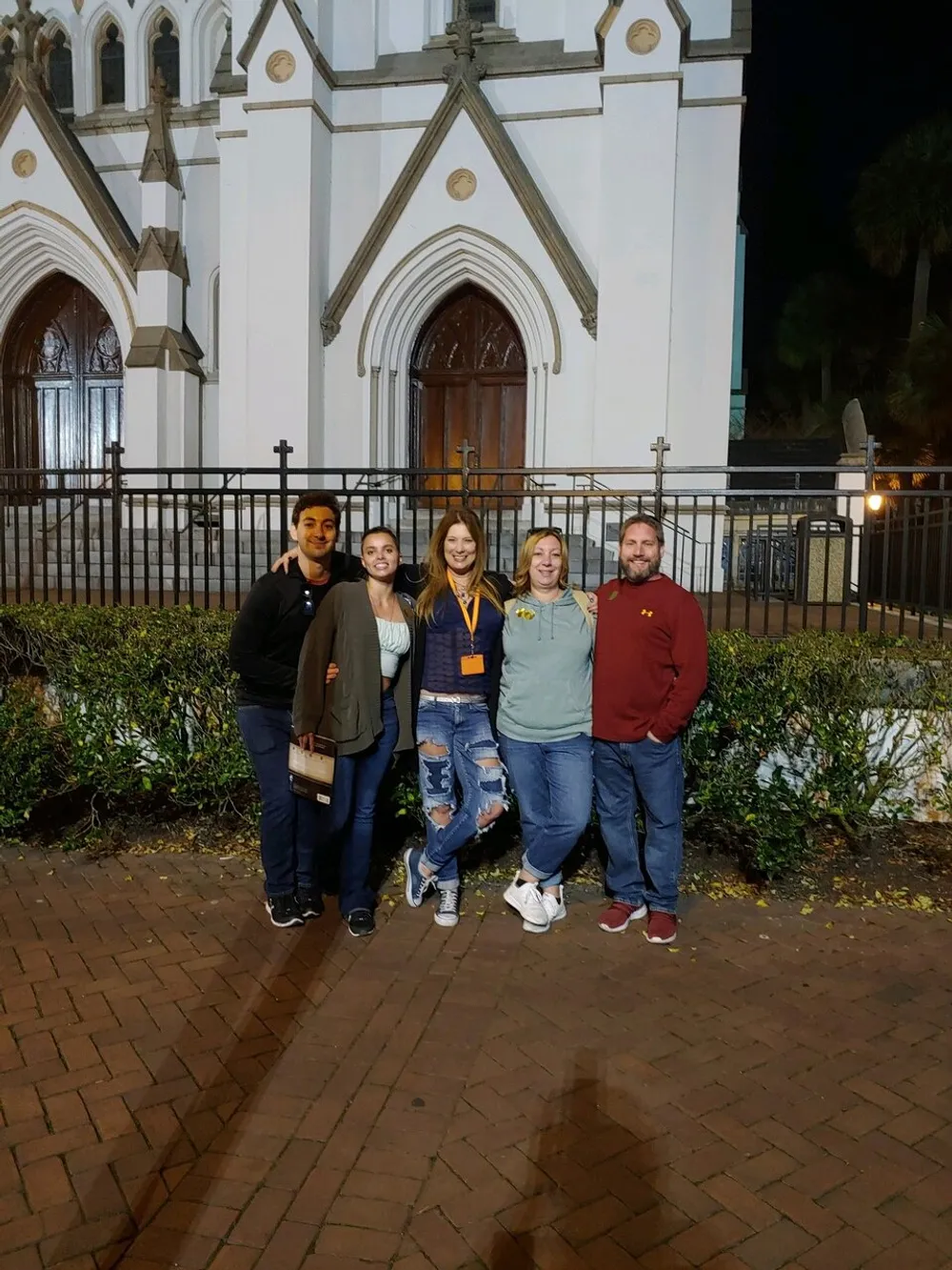 Five individuals are posing for a photo at night in front of a church with gothic architectural features