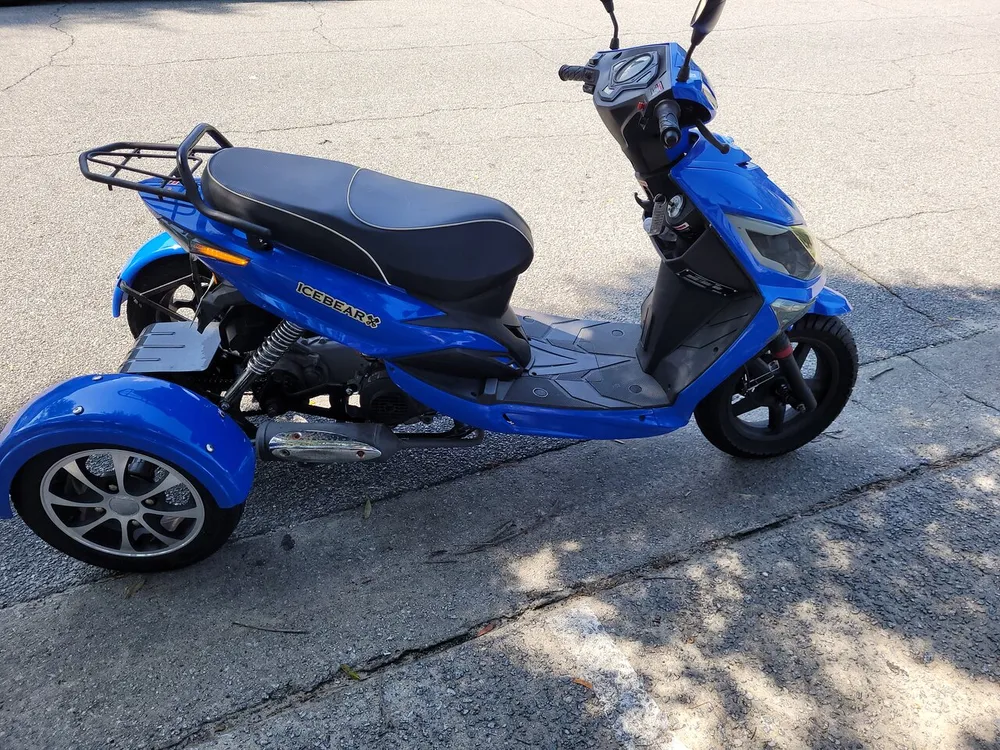 The image shows a blue three-wheeled scooter branded as ICEBEAR parked on an asphalt surface in daylight