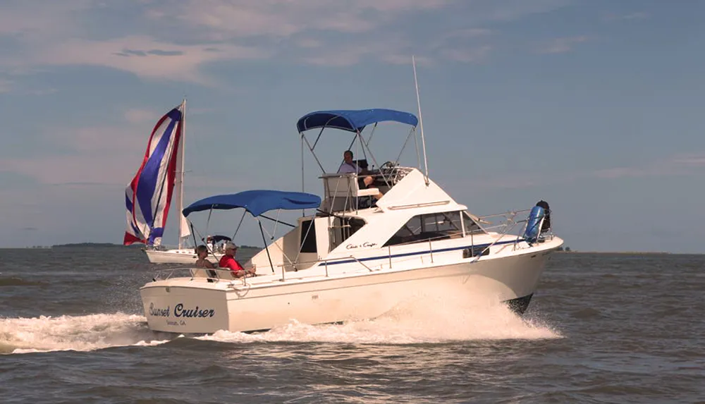 A motorboat named Coastal Cruiser sails on the water with people on board displaying a blue canopy for shade and a flag fluttering at the stern