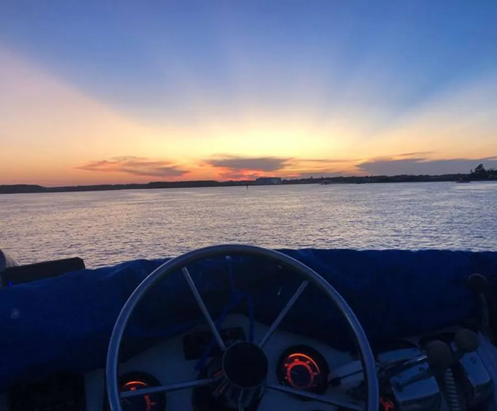 A serene sunset view over the water as seen from behind a boats steering wheel