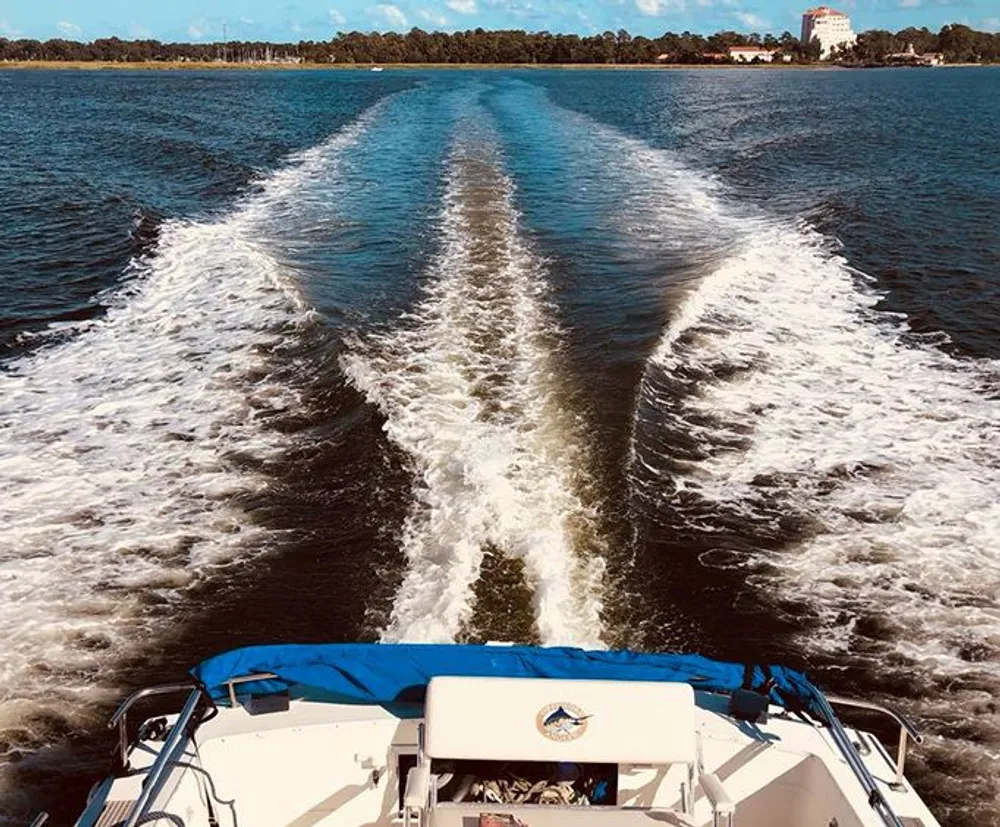 The image shows the view from the stern of a moving boat creating a V-shaped wake on a body of water under a clear sky