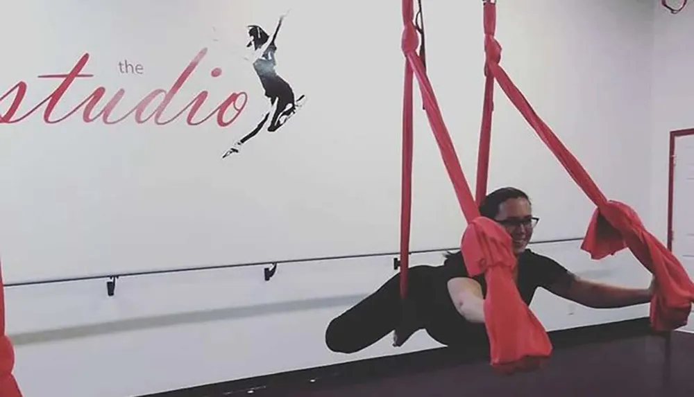 A person is practicing an aerial silk move in a studio with the studio written on the wall alongside a silhouette of a dancer