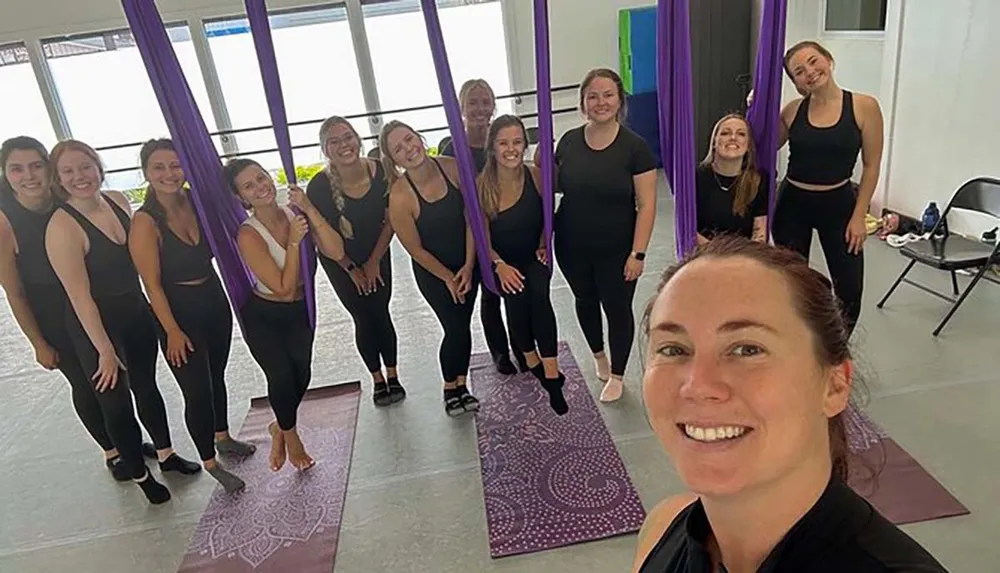 A group of smiling people in a bright studio with purple aerial silks taking a selfie together