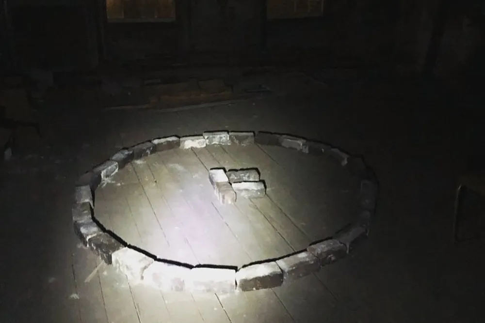 The image shows a dimly-lit room with a circular pattern of bricks laid out on the floor