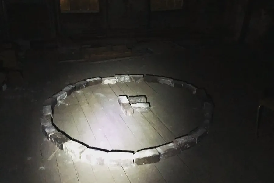 The image shows a dimly-lit room with a circular pattern of bricks laid out on the floor.