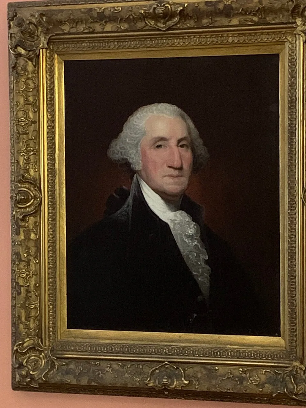 The image shows a framed portrait of a historical figure with white hair and a black coat set against a dark background within an ornate gold frame