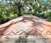 The image shows a sunny pathway lined with brick pavers leading through a park with dangling Spanish moss from large oak trees with a metal plate in the foreground that reads Orleans Square