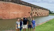 A group of five people stands smiling in front of an old brick fortification surrounded by a moat.