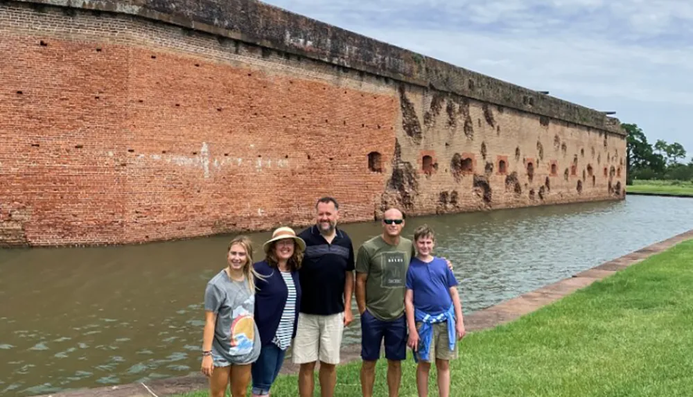 A group of five people stands smiling in front of an old brick fortification surrounded by a moat