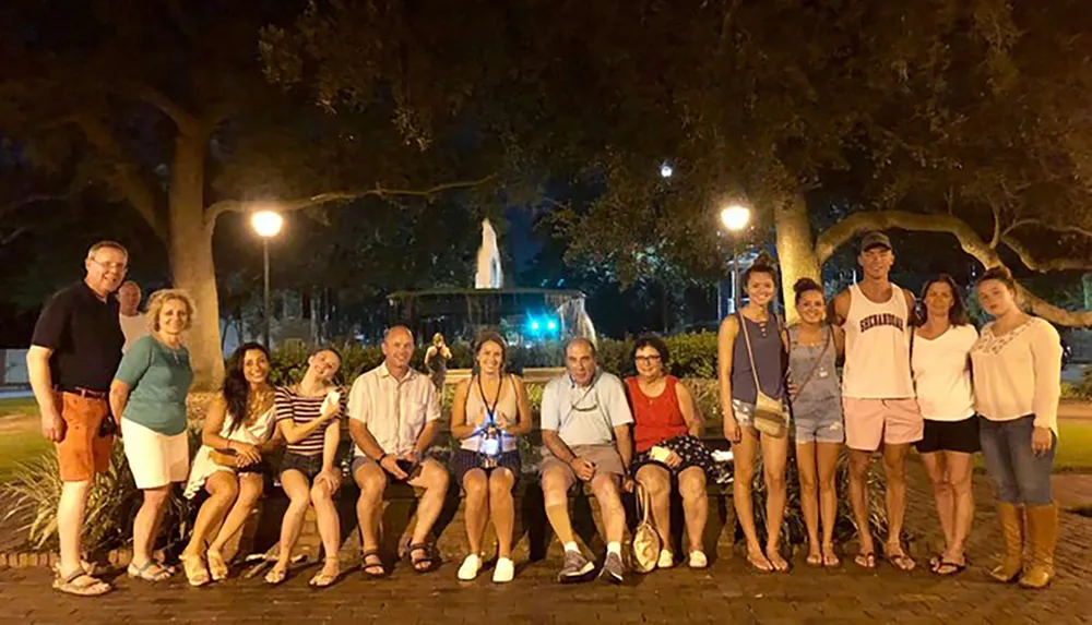 A group of people are posing for a nighttime photo in a park with a fountain illuminated in the background