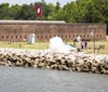 This image shows a historic fort with a large Texas flag flying people nearby and a cannon firing creating a large cloud of smoke along the rocky shoreline