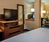 This image showcases a well-appointed hotel room with a large bed work desk and television decorated in warm and inviting tones