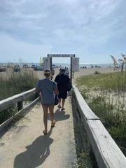 People are walking on a sandy boardwalk leading to North Beach on a sunny day.