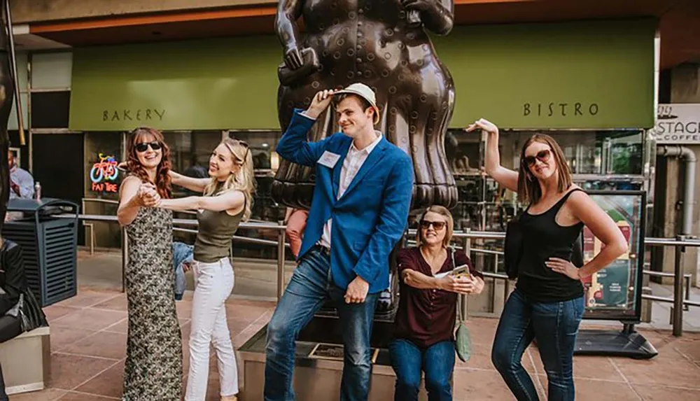 A group of people is posing playfully in front of a large chocolate bunny statue with one person pretending to tip the statues top hat