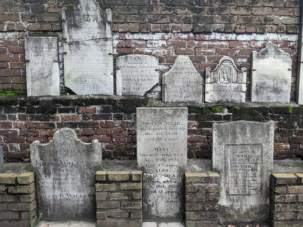 This image shows a collection of weathered historical gravestones mounted onto a brick wall