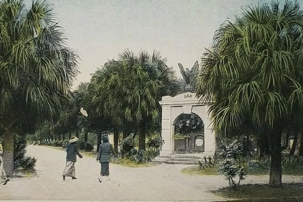 Two individuals are meandering down a palm-lined pathway toward a white stone archway in what appears to be an old hand-colored photograph