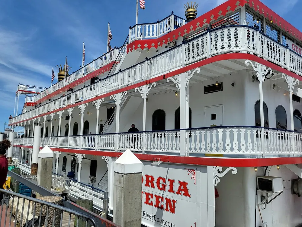 The image shows a large ornately decorated riverboat with multiple decks named Georgia Queen docked under a clear blue sky