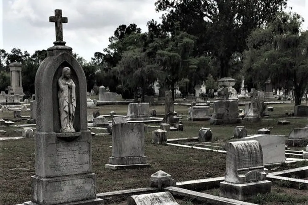 The image shows a serene overcast cemetery with a variety of grave markers and a prominent statue within an arch-shaped monument