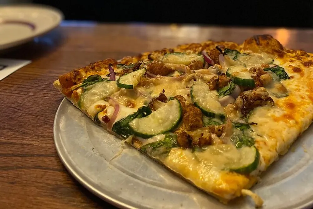 This is an image of a partially eaten pizza with toppings like onions spinach zucchini and chicken on a metal serving tray