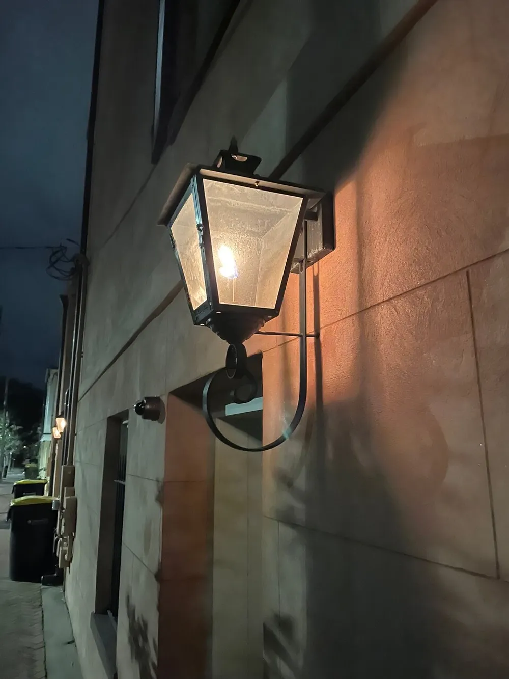 An illuminated lantern-style light fixture casts a warm glow on a buildings exterior wall at dusk