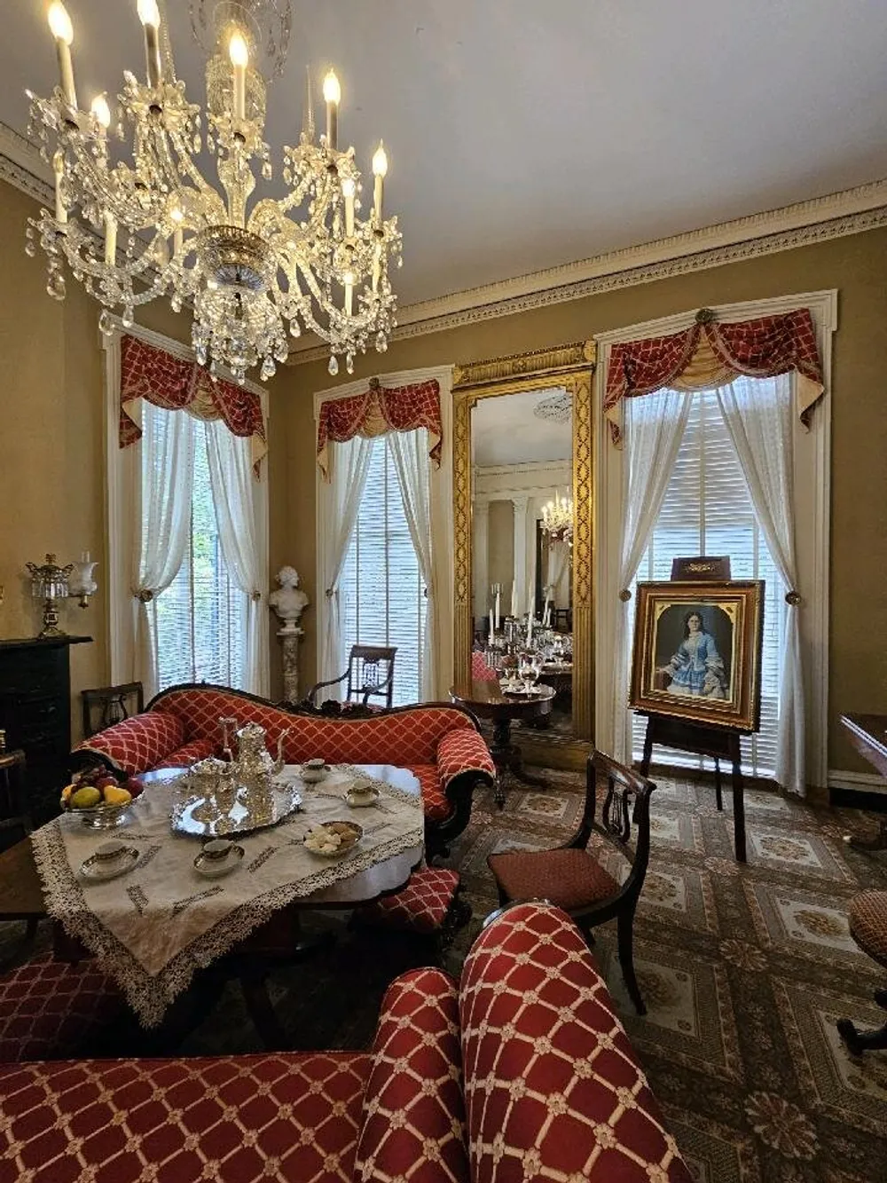 An elegant traditional drawing room featuring a crystal chandelier patterned furniture and classical curtains with a portrait prominently displayed