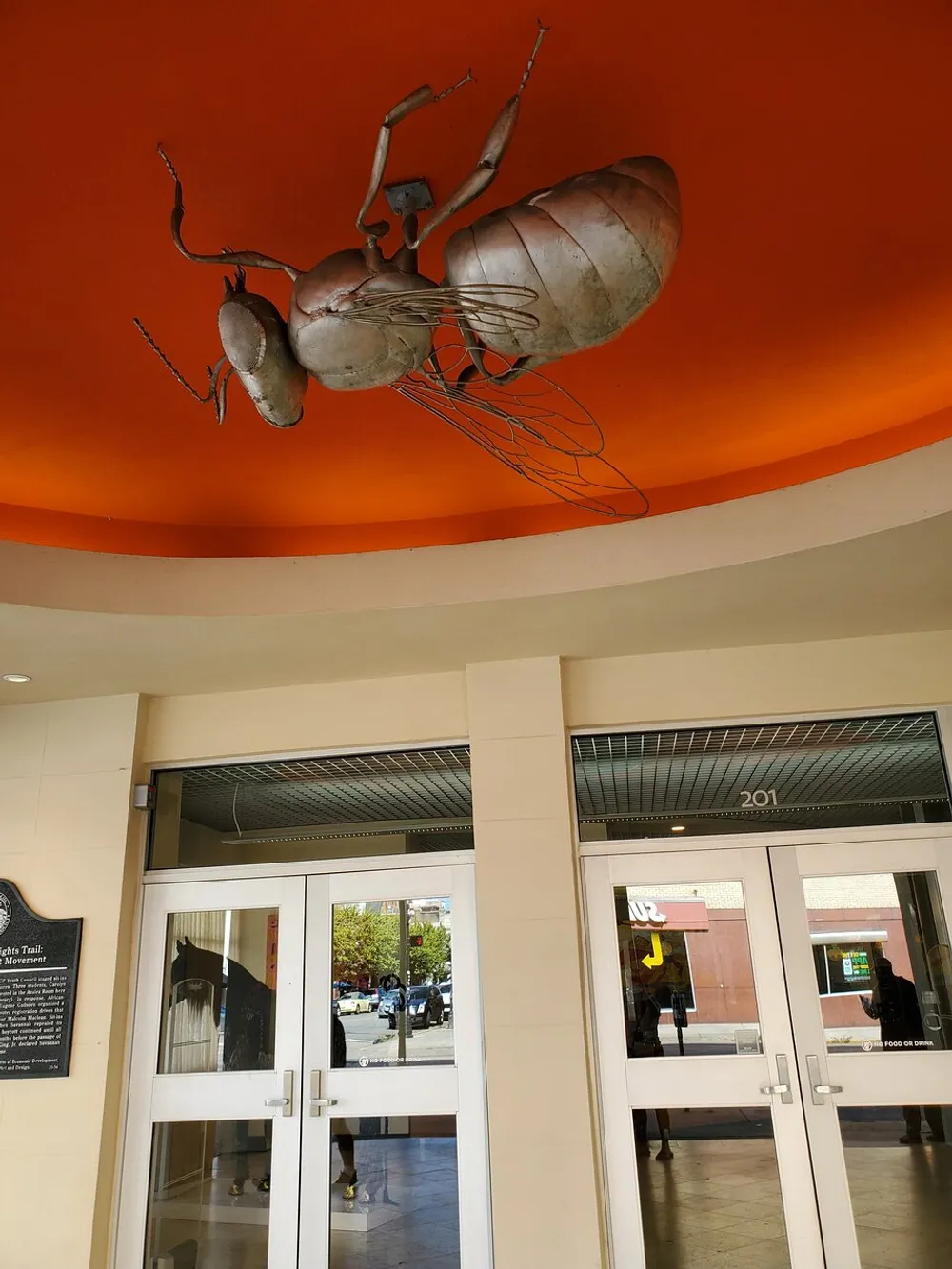 A large metal sculpture of an ant hangs from an orange ceiling above the entrance to a building