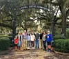 A group of people is posing for a photo in front of the entrance to Laurel Grove Cemetery which is adorned with Spanish moss-draped trees