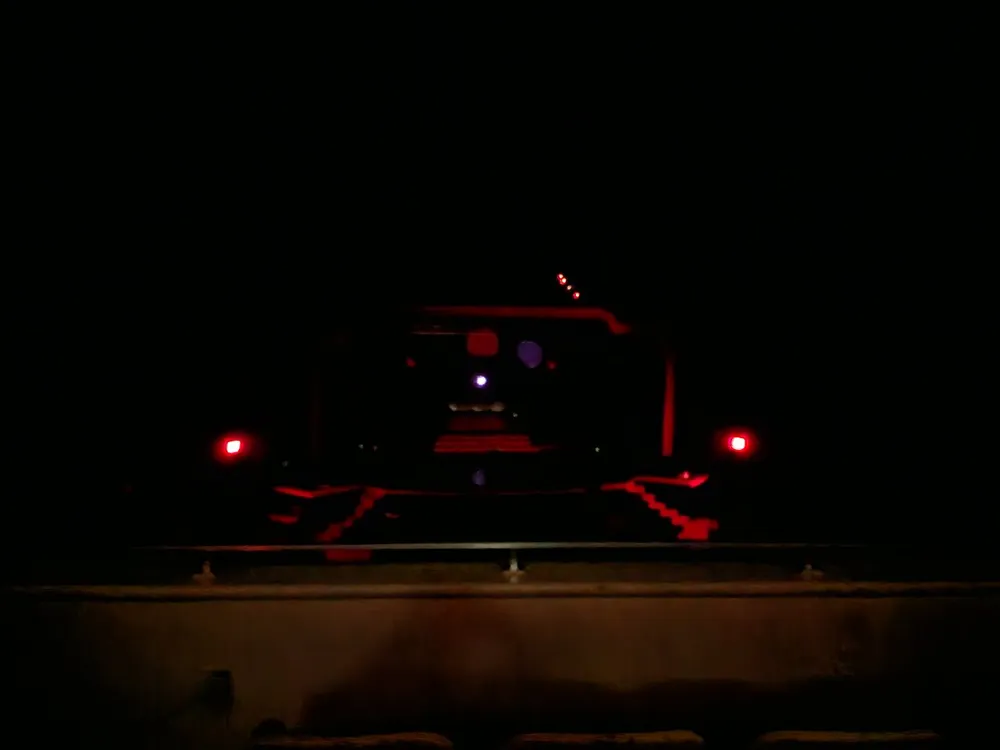 The image shows a dark scene illuminated by the red and white lights of a vehicle that is either parked or approaching creating an ominous atmosphere