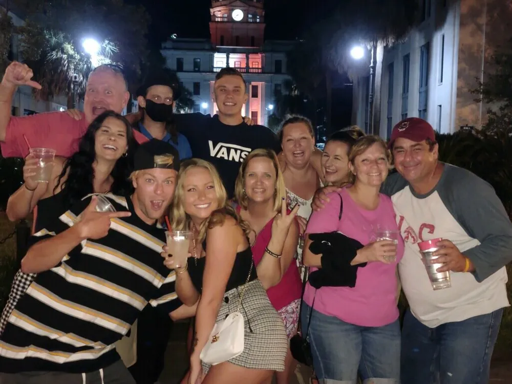 A group of people appear to be having a fun night out posing for a photo with drinks in hand and a lit building in the background