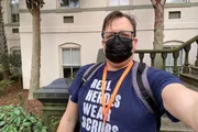 A person is taking a selfie while wearing a mask, glasses, a T-shirt that reads 