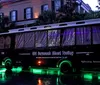 A black trolley with green and purple lights is parked on a wet street at dusk advertising the Old Savannah Ghost Trolley tour