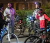 A group of people with bicycles are standing together at night engaged in a conversation