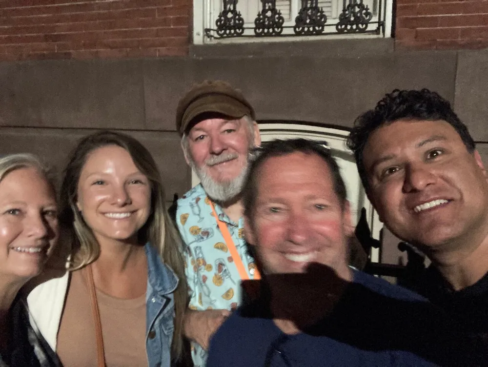 A group of five cheerful people are posing closely together for a selfie at night with building details partially visible in the background