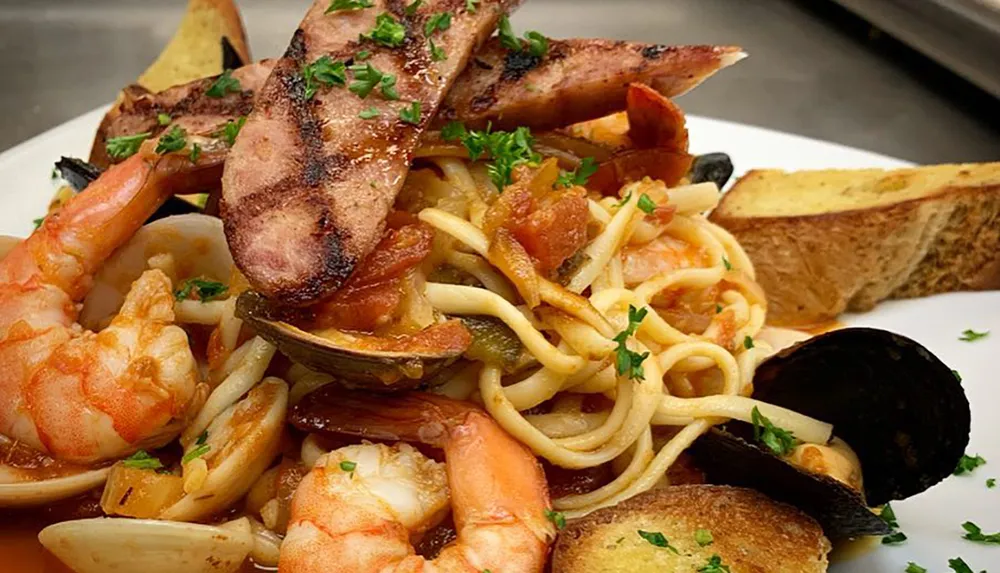 The image shows a seafood pasta dish with shrimp mussels and spicy sausage garnished with parsley and served with slices of toasted bread