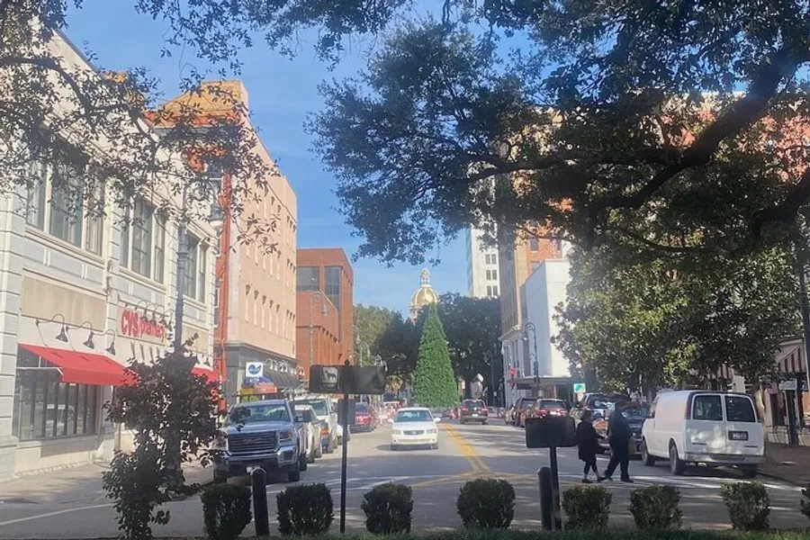 The image shows a bustling city street with traffic, pedestrians, and a large Christmas tree indicating holiday season, set against a backdrop of mixed architecture and clear skies.