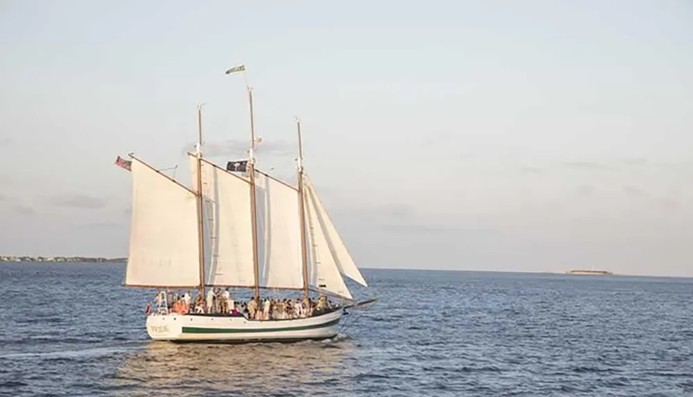 A group of people sails on a traditional schooner near the coast in calm sea conditions under a clear sky