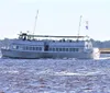 A passenger boat sails on a body of water with a few people visible on the upper deck