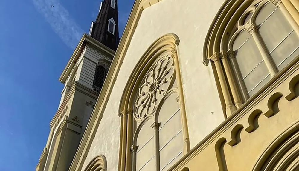 The image displays the exterior of a building with architectural features suggesting it could be a church characterized by arched windows a Gothic rose window and a steeple against a clear blue sky
