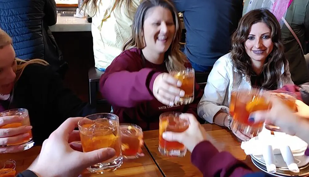 A group of people are happily toasting with amber-colored drinks at a social gathering