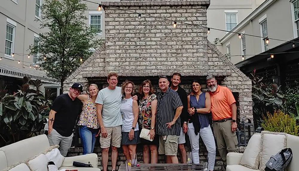 A group of people are posing for a photo in a cozy outdoor patio with string lights and stone architecture in the background