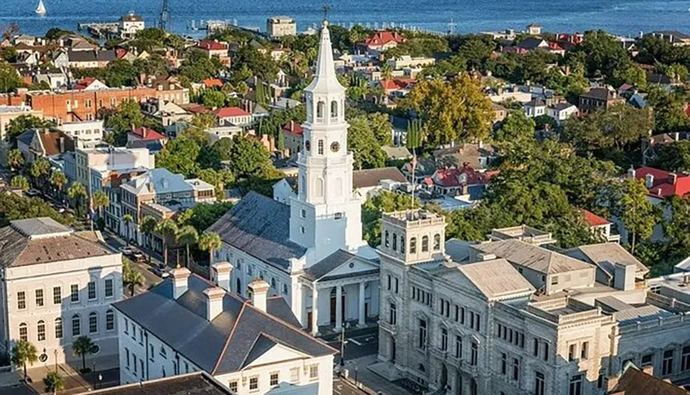 The image showcases an aerial view of a coastal town with a prominent white church spire rising above historic buildings and lush greenery with a glimpse of the water in the background