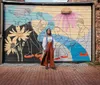 A woman stands in front of a colorful garage door mural featuring abstract human figures and sunflowers