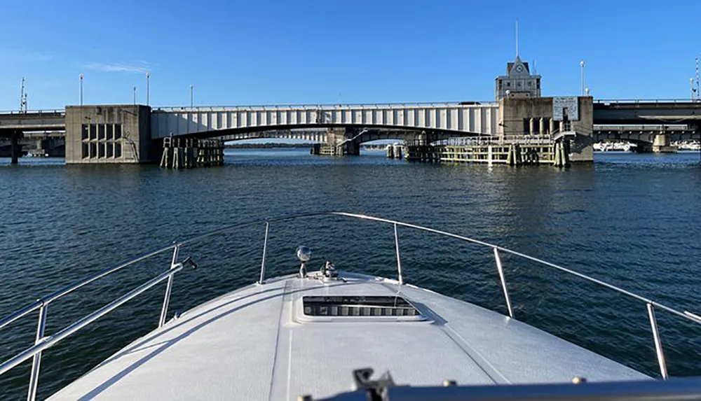 The image shows the view from the bow of a boat approaching a large drawbridge over a body of water on a sunny day