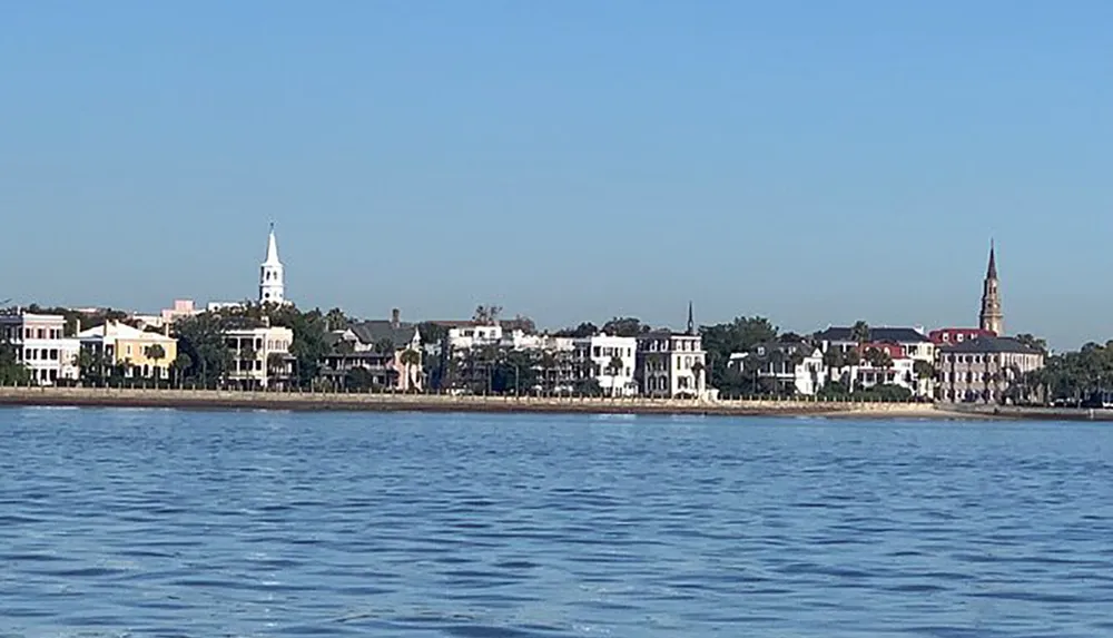 The image shows a calm body of water with a skyline of white buildings and two prominent church spires against a clear blue sky