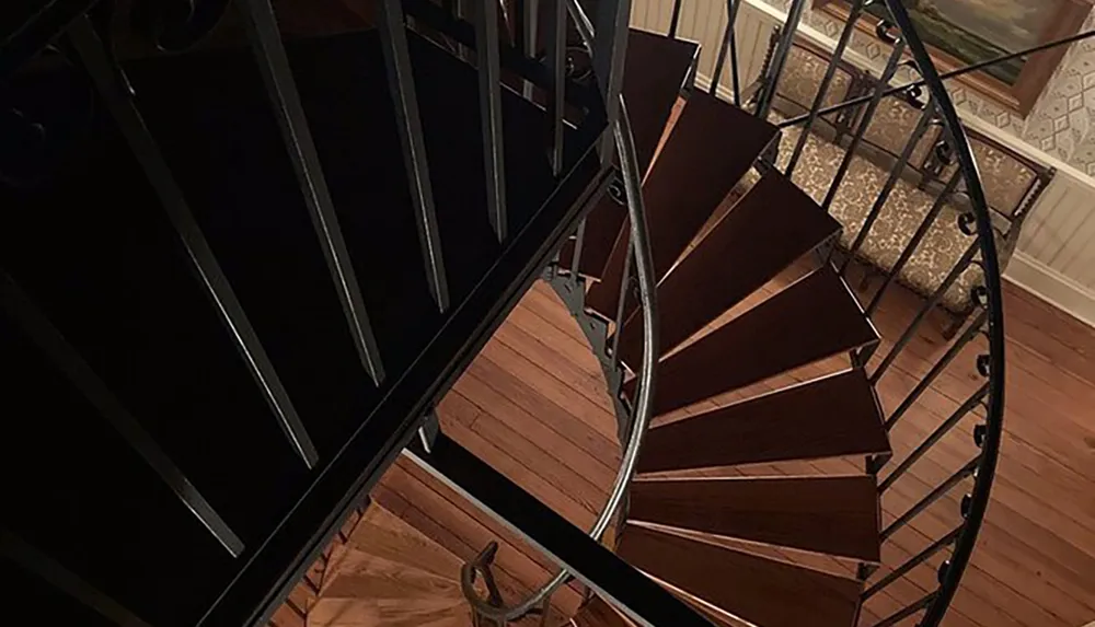 This image shows a top-down view of a wooden spiral staircase with wrought-iron railings inside a house